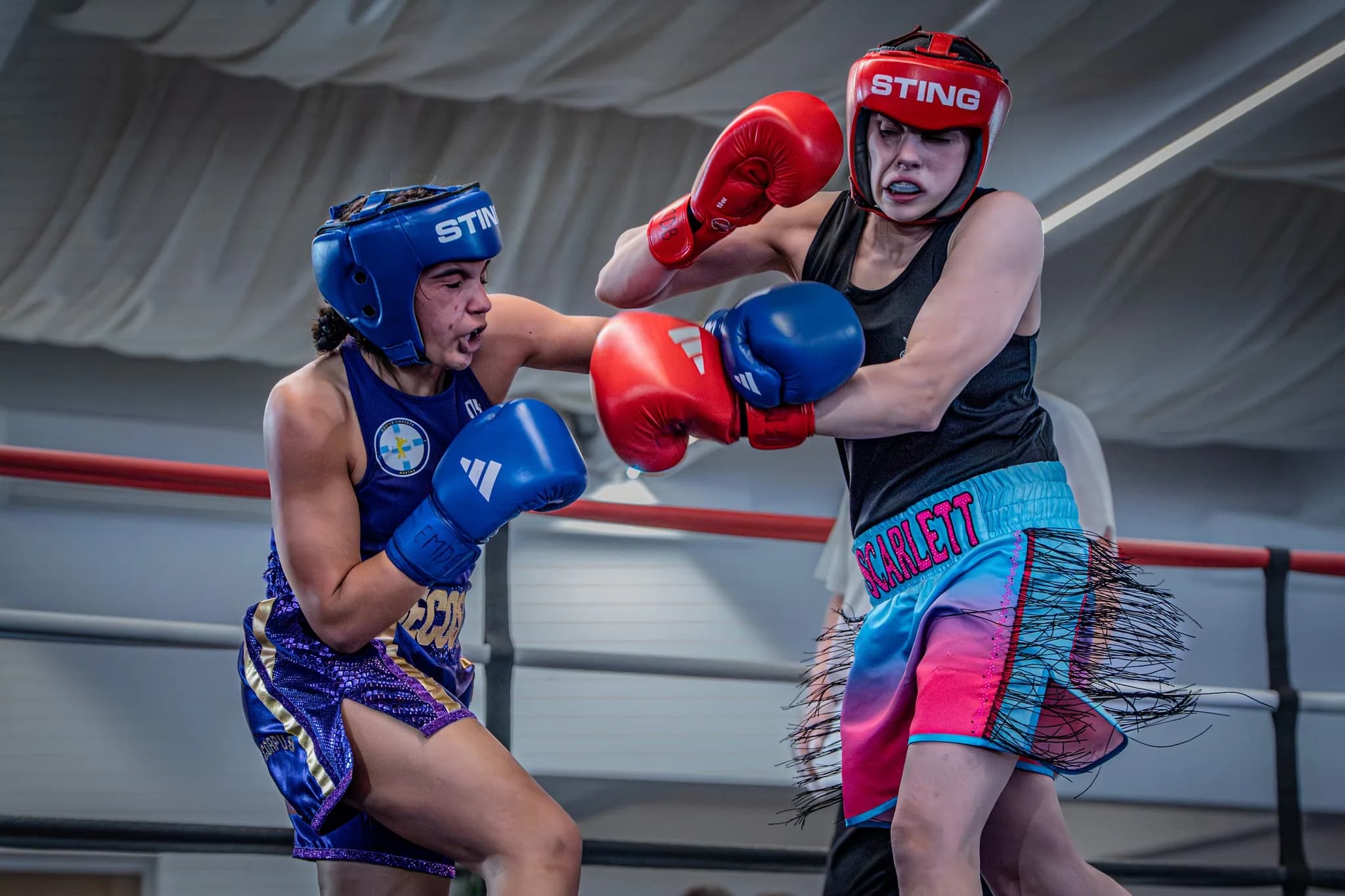 Youth boxing bout with one boxer throwing a glove toward her opponent's guard.