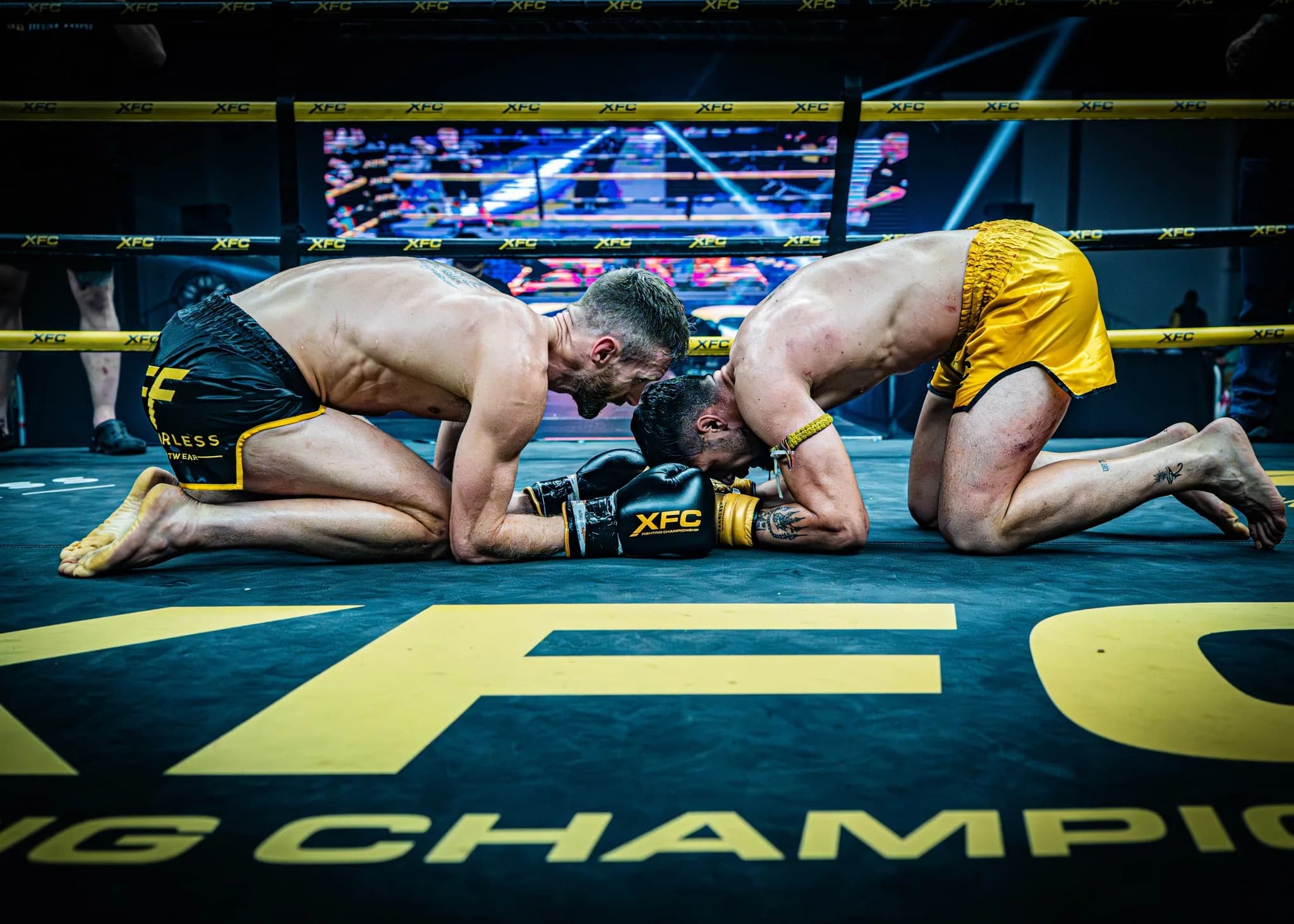 Two fighters kneeling together on the canvas in a respectful post-bout moment.